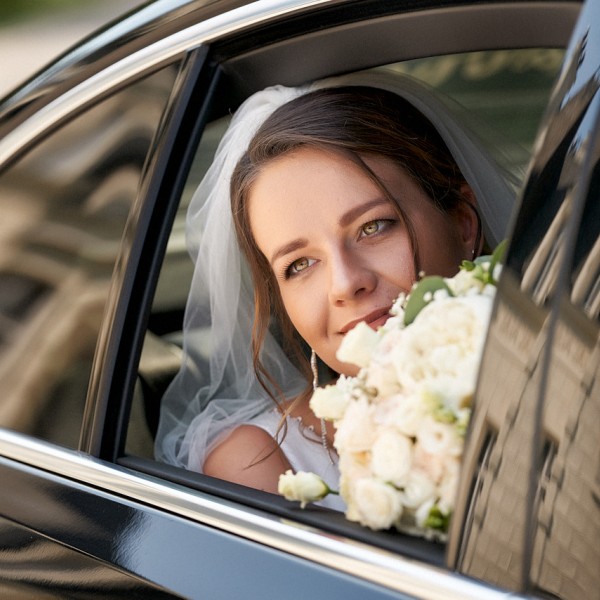 Pohlad na nevestu so svadobnou kyticou cez okno auta