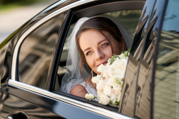 Pohlad na nevestu so svadobnou kyticou cez okno auta