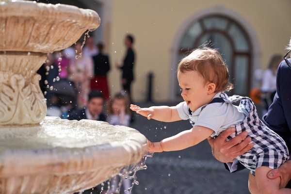 Chlapcek hrajuci sa s kvapkami vody vo fontane na nadvori zamku Simak v Pezinku
