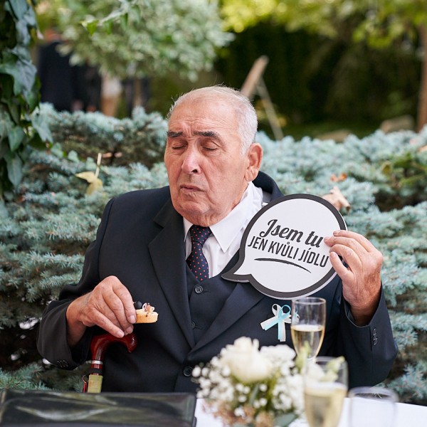 Momentka stareho otca nevesty drziaceho vtipnu tabulku, ze je na svadbe iba kvoli jedlu 