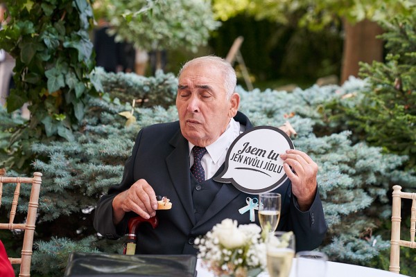 Momentka stareho otca nevesty drziaceho vtipnu tabulku, ze je na svadbe iba kvoli jedlu 